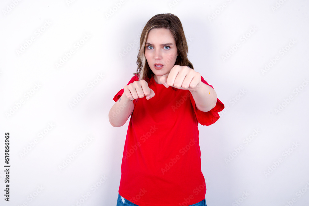 young caucasian woman wearing red T-shirt over white background Punching fist to fight, aggressive and angry attack, threat and violence young caucasian woman wearing red T-shirt over white background Punching fist to fight, aggressive and angry attack, threat and violence
