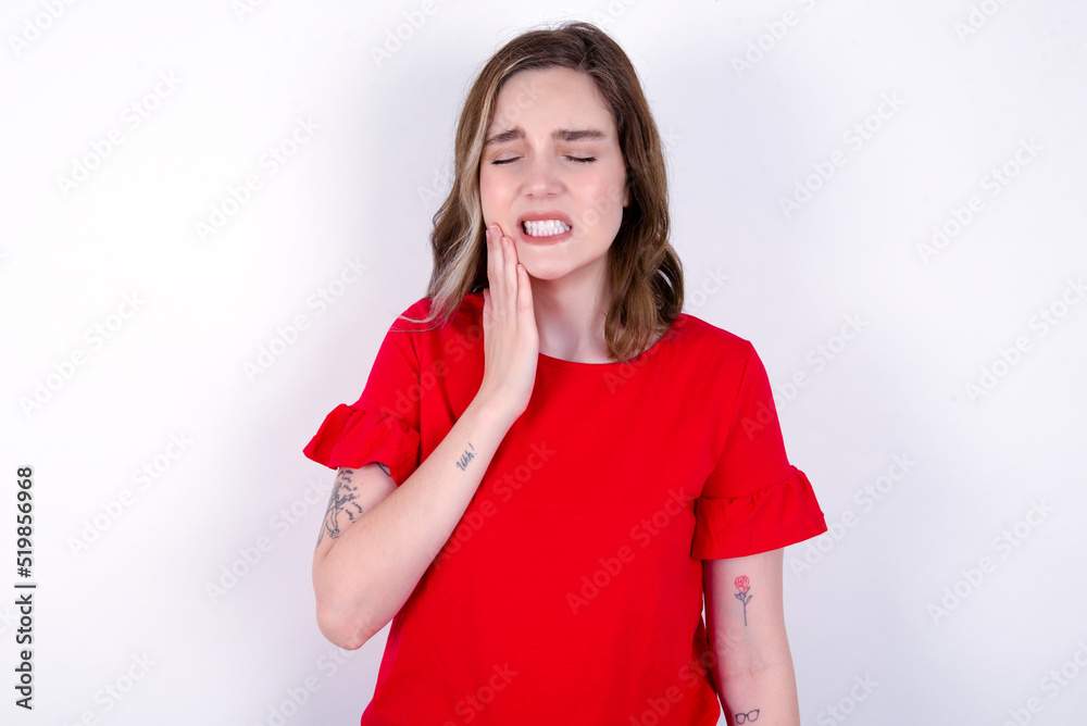 young caucasian woman wearing red T-shirt over white background touching mouth with hand with painful expression because of toothache or dental illness on teeth. young caucasian woman wearing red T-shirt over white background touching mouth with hand with painful expression because of toothache or dental illness on teeth.