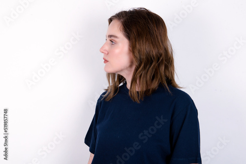 Close up side profile photo young caucasian woman wearing black T-shirt over white background not smiling attentive listen concentrated