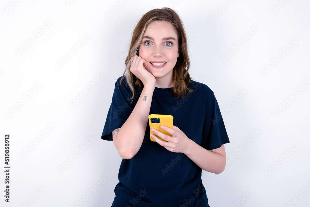 Joyous young caucasian woman wearing black T-shirt poses with mobile phone device, types text message on modern smartphone, watches funny video during free time, enjoys good internet connection, Joyous young caucasian woman wearing black T-shirt poses with mobile phone device, types text message on modern smartphone, watches funny video during free time, enjoys good internet connection,