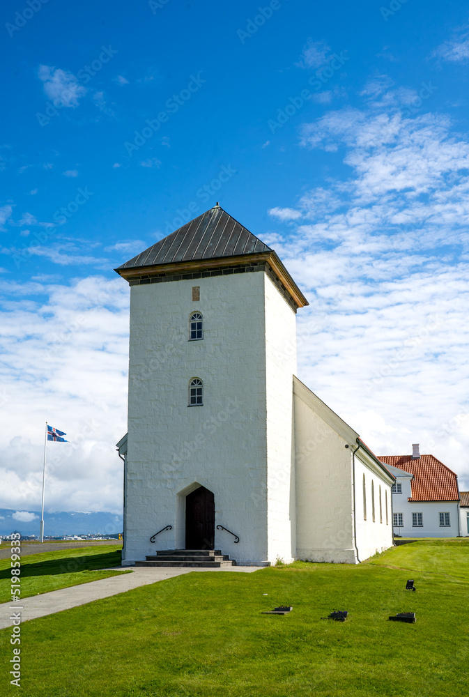 Álftanes, Iceland - July 1, 2022 Vertical view of the church of the Bessastadir, a modest group of white, red-roofed buildings that is the official residence of the president of Iceland. Álftanes, Iceland - July 1, 2022 Vertical view of the church of the Bessastadir, a modest group of white, red-roofed buildings that is the official residence of the president of Iceland.