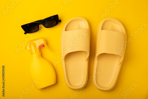 Flat lay composition with beach accessories on yellow background. Beach slippers, sunglasses and sunscreen.SPF sun protection.Space for copy.Place for text.Vacation concept.