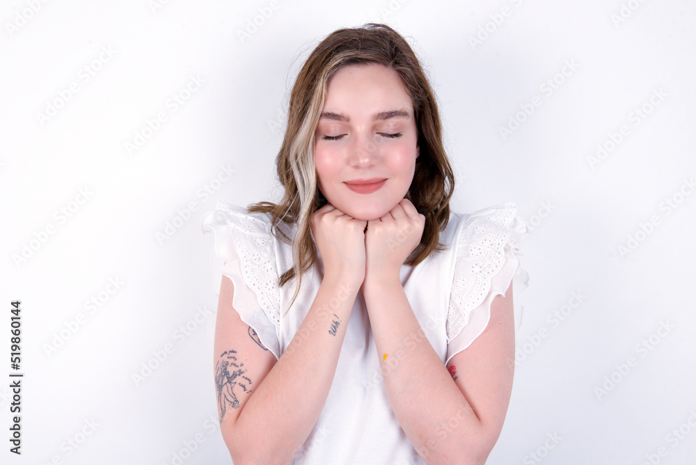 Cheerful young caucasian woman wearing white T-shirt over white background has shy satisfied expression, smiles broadly, shows white teeth, People emotions Cheerful young caucasian woman wearing white T-shirt over white background has shy satisfied expression, smiles broadly, shows white teeth, People emotions