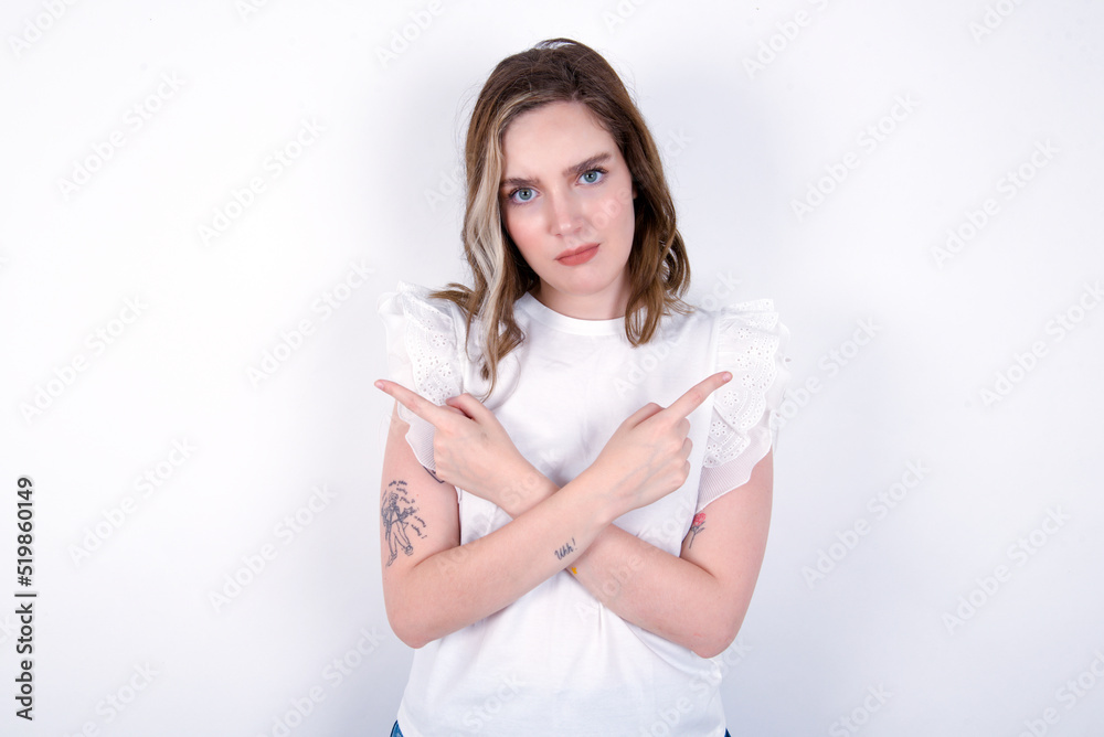 Serious young caucasian woman wearing white T-shirt over white background crosses hands and points at different sides hesitates between two items. Hard decision concept Serious young caucasian woman wearing white T-shirt over white background crosses hands and points at different sides hesitates between two items. Hard decision concept
