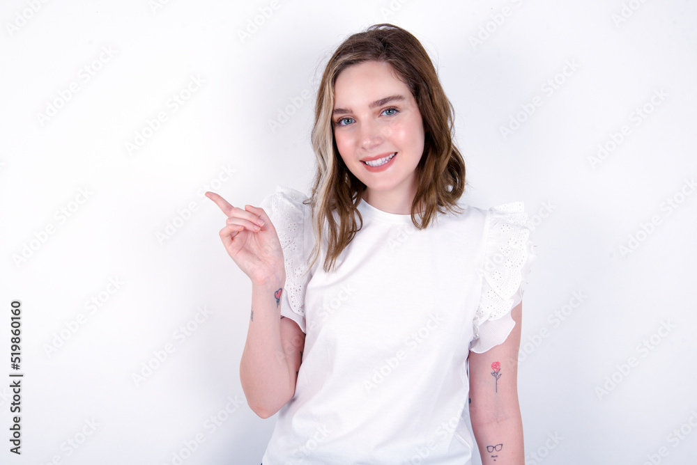young caucasian woman wearing white T-shirt over white background points to side on blank space demonstrates advertisement. People and promotion concept young caucasian woman wearing white T-shirt over white background points to side on blank space demonstrates advertisement. People and promotion concept
