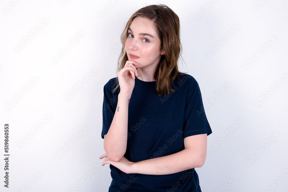 young caucasian woman wearing black T-shirt over white background looking confident at the camera smiling with crossed arms and hand raised on chin. Thinking positive. young caucasian woman wearing black T-shirt over white background looking confident at the camera smiling with crossed arms and hand raised on chin. Thinking positive.