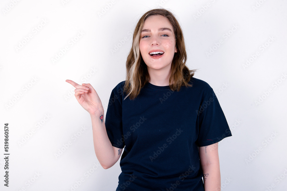 young caucasian woman wearing black T-shirt over white background laughs happily points away on blank space demonstrates shopping discount offer, excited by good news or unexpected sale. young caucasian woman wearing black T-shirt over white background laughs happily points away on blank space demonstrates shopping discount offer, excited by good news or unexpected sale.