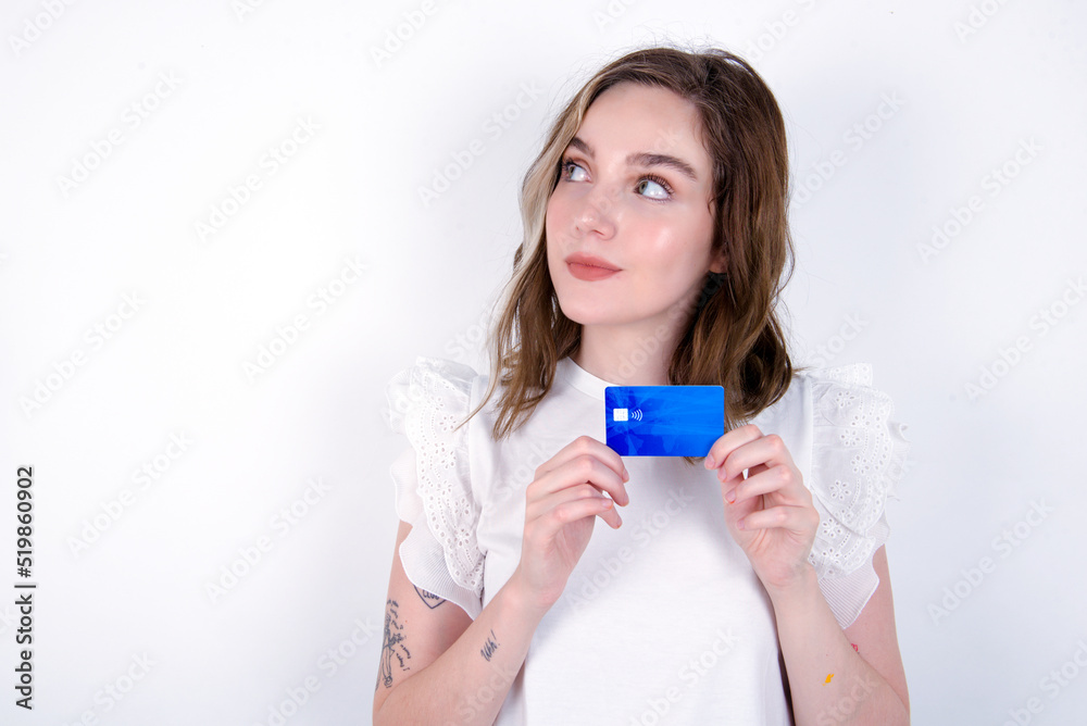 Photo of cheerful young caucasian woman wearing white T-shirt over white background hold debit card look empty space