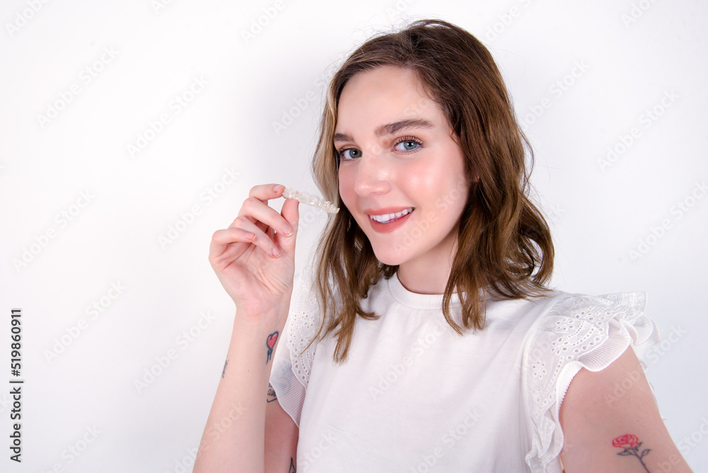 young caucasian woman wearing white T-shirt over white background make selfie holding an invisible braces aligner, recommending this new treatment. Dental healthcare concept. young caucasian woman wearing white T-shirt over white background make selfie holding an invisible braces aligner, recommending this new treatment. Dental healthcare concept.