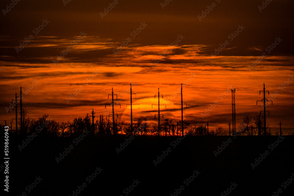 Sunset of the big sun in the evening against the background of the horizon sky and electric antennas