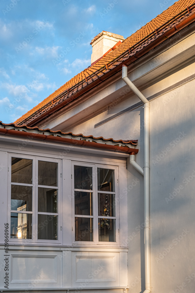 Bottom - up view of tiled roof of white building with blue sky in the background on a sunny summer day. Bottom - up view of tiled roof of white building with blue sky in the background on a sunny summer day.