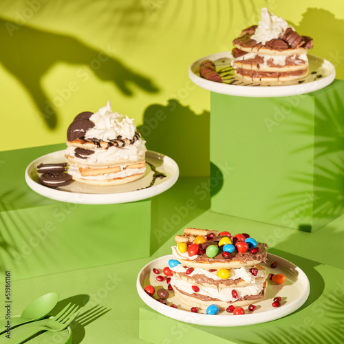Pancakes with whipped cream, chocolates and berries. Pancakes with different toppings. Morning tasty homemade breakfast, stack of fluffy and delicious pancakes. Green, tropical background. Close up.