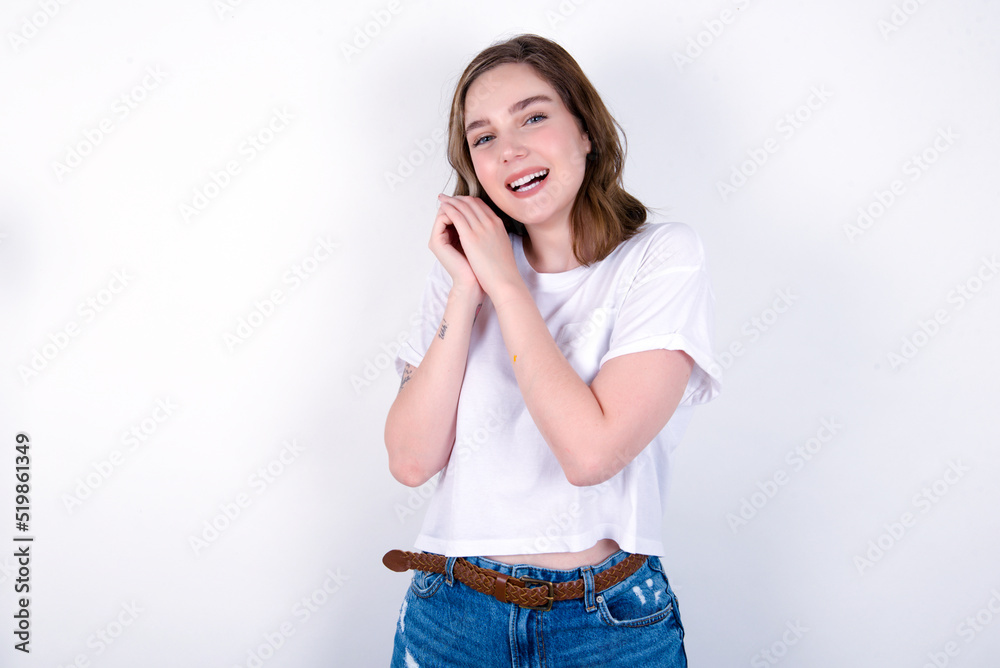 Dreamy young caucasian woman wearing white T-shirt over white background with pleasant expression, closes eyes, keeps hands crossed near face, thinks about something pleasant Dreamy young caucasian woman wearing white T-shirt over white background with pleasant expression, closes eyes, keeps hands crossed near face, thinks about something pleasant