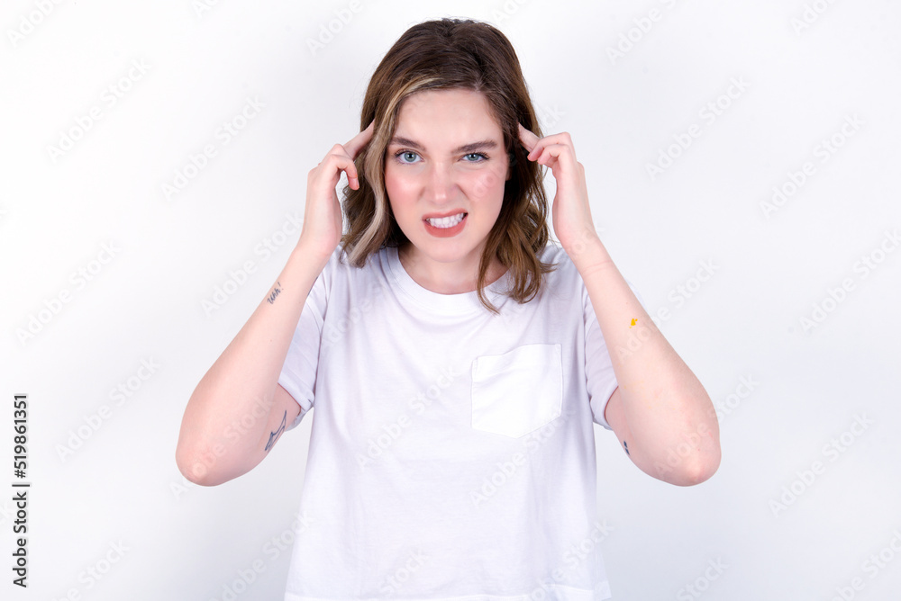 young caucasian woman wearing white T-shirt over white background concentrating hard on an idea with a serious look, thinking with both index fingers pointing to forehead. young caucasian woman wearing white T-shirt over white background concentrating hard on an idea with a serious look, thinking with both index fingers pointing to forehead.