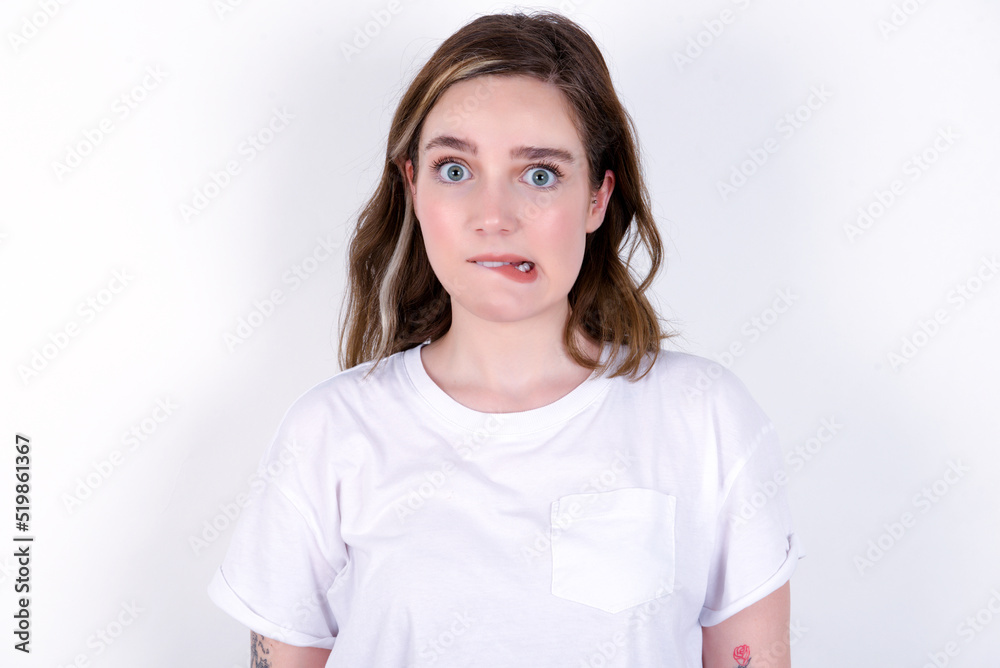 young caucasian woman wearing white T-shirt over white background being nervous and scared biting lips looking camera with impatient expression, pensive. young caucasian woman wearing white T-shirt over white background being nervous and scared biting lips looking camera with impatient expression, pensive.