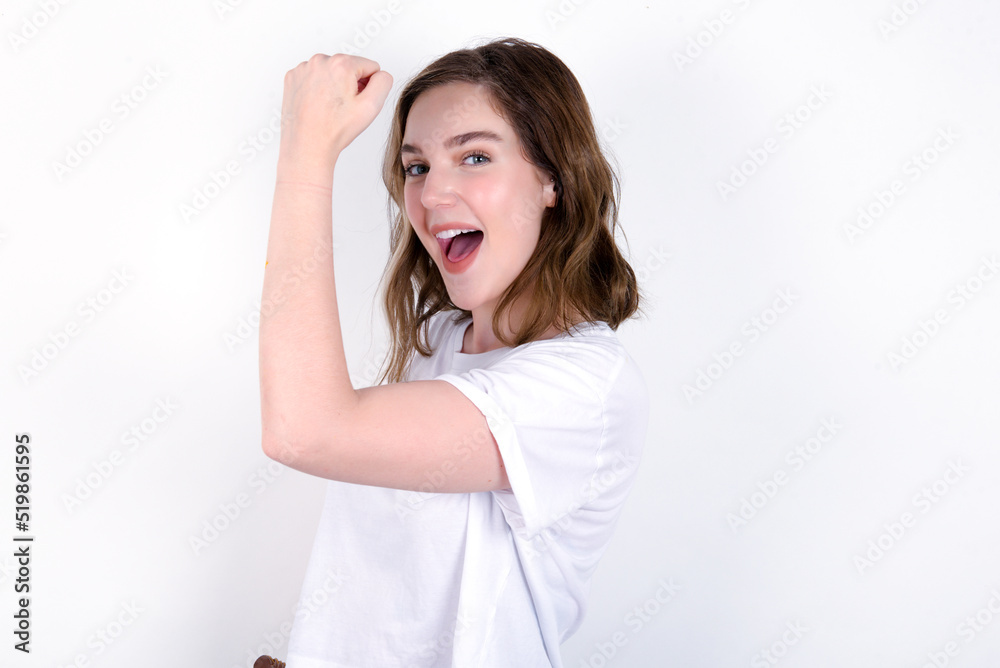 Overjoyed young caucasian woman wearing white T-shirt over white background glad to receive good news, clenching fist and making winning gesture. Overjoyed young caucasian woman wearing white T-shirt over white background glad to receive good news, clenching fist and making winning gesture.