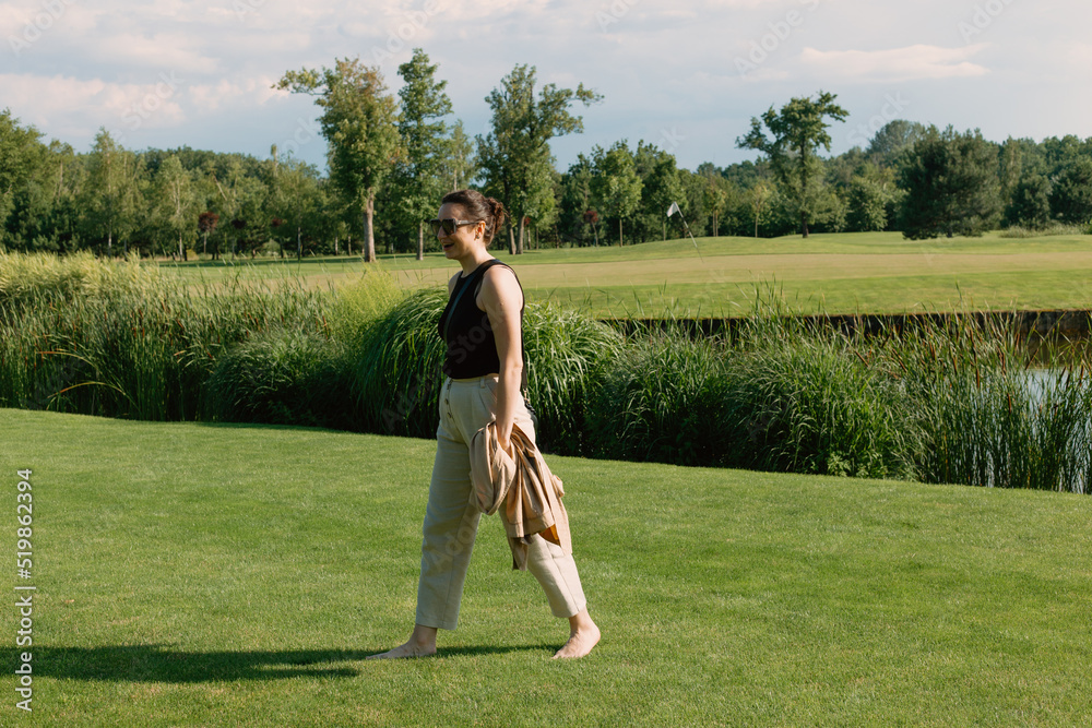 Beautiful girl walking barefoot on the green grass in the park on a sunny day Beautiful girl walking barefoot on the green grass in the park on a sunny day