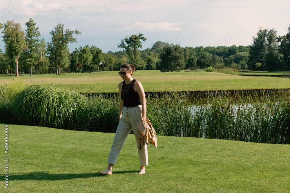 Beautiful girl walking barefoot on the green grass in the park on a sunny day