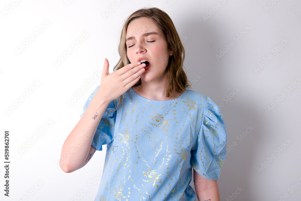 Sleepy young caucasian woman wearing blue T-shirt over white background yawning with messy hair, feeling tired after sleepless night, yawning, covering mouth with palm. Sleepy young caucasian woman wearing blue T-shirt over white background yawning with messy hair, feeling tired after sleepless night, yawning, covering mouth with palm.