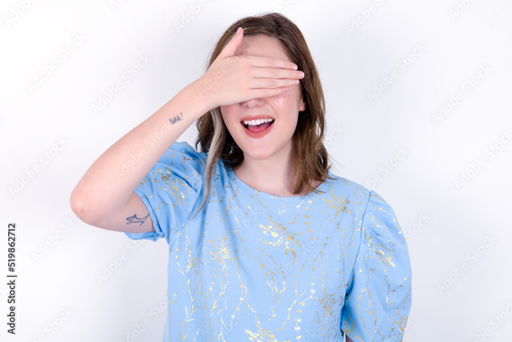 Happy young caucasian woman wearing blue T-shirt over white background closing eyes with hand going to see surprise prepared by friend standing and smiling in anticipation for something wonderful. Happy young caucasian woman wearing blue T-shirt over white background closing eyes with hand going to see surprise prepared by friend standing and smiling in anticipation for something wonderful.