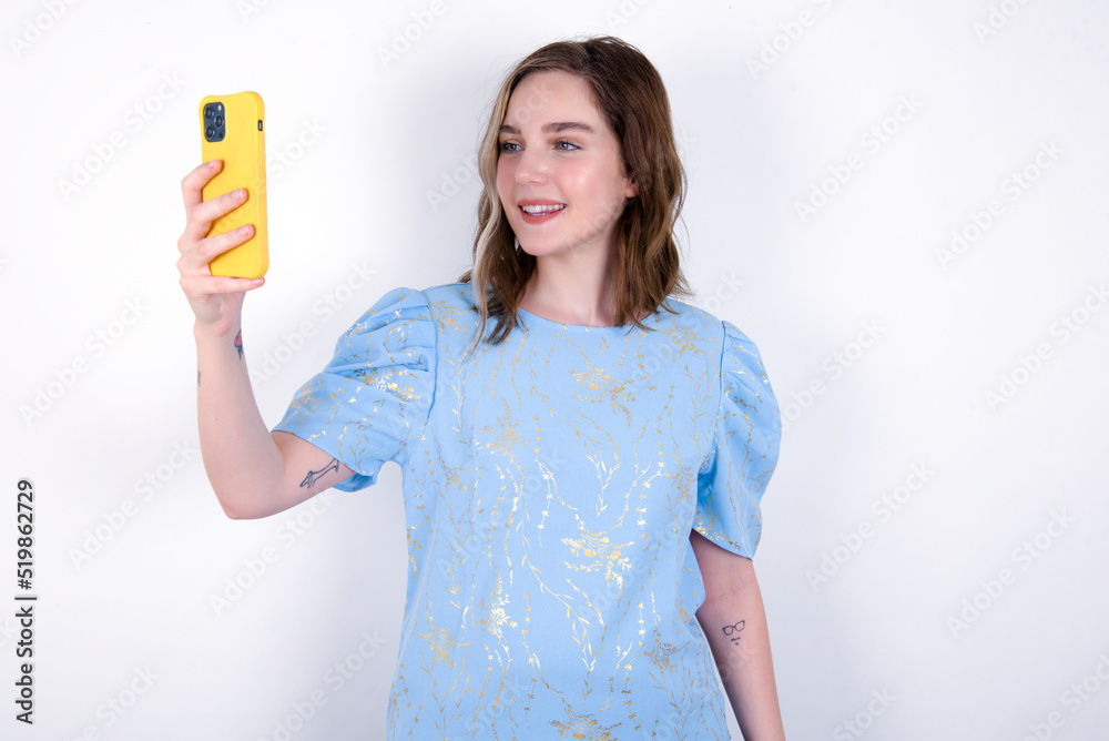 Isolated shot of pleased cheerful young caucasian woman wearing blue T-shirt over white background , makes selfie with mobile phone. People, technology and leisure concept Isolated shot of pleased cheerful young caucasian woman wearing blue T-shirt over white background , makes selfie with mobile phone. People, technology and leisure concept