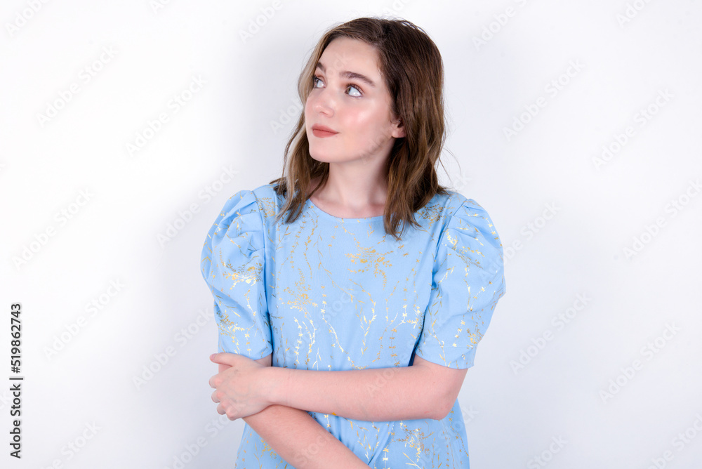 Pleased young caucasian woman wearing blue T-shirt over white background keeps hands crossed over chest looks happily aside Pleased young caucasian woman wearing blue T-shirt over white background keeps hands crossed over chest looks happily aside