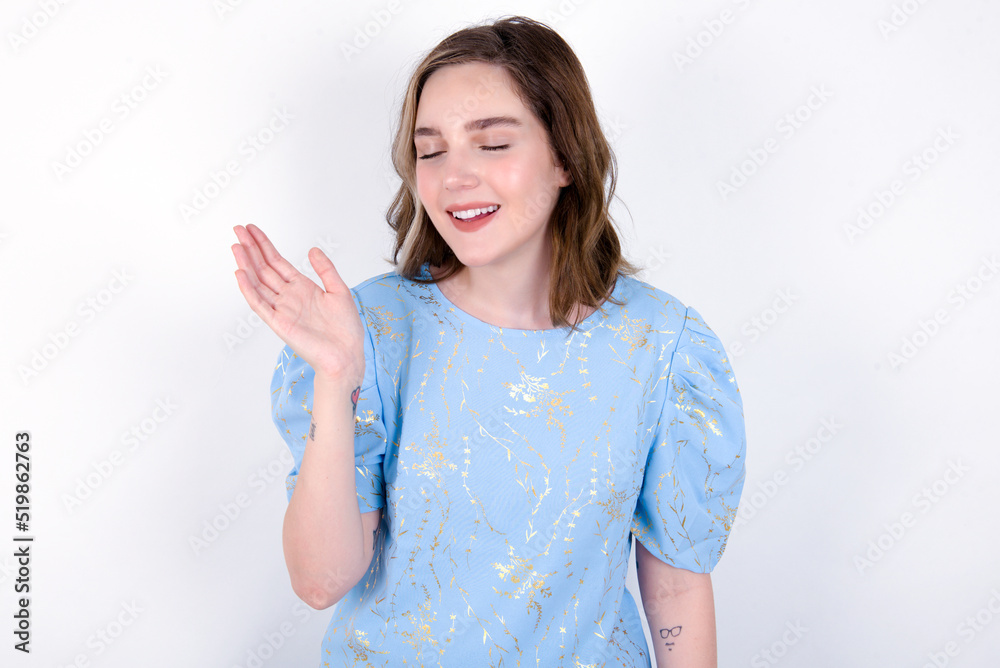 Overjoyed successful young caucasian woman wearing blue T-shirt over white background raises palm and closes eyes in joy being entertained by friends Overjoyed successful young caucasian woman wearing blue T-shirt over white background raises palm and closes eyes in joy being entertained by friends