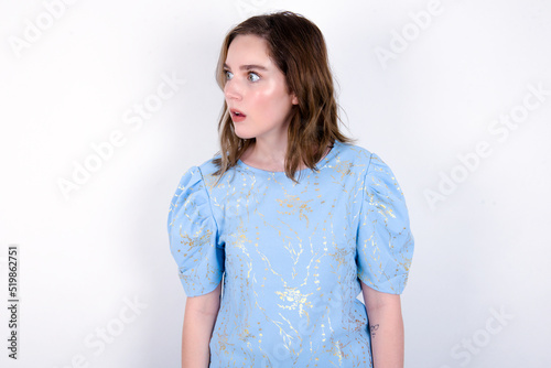 young caucasian woman wearing blue T-shirt over white background stares aside with wondered expression has speechless expression. Embarrassed model looks in surprise