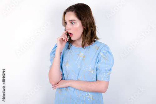 Astonished young caucasian woman wearing blue T-shirt over white background looks aside surprisingly with opened mouth. photo