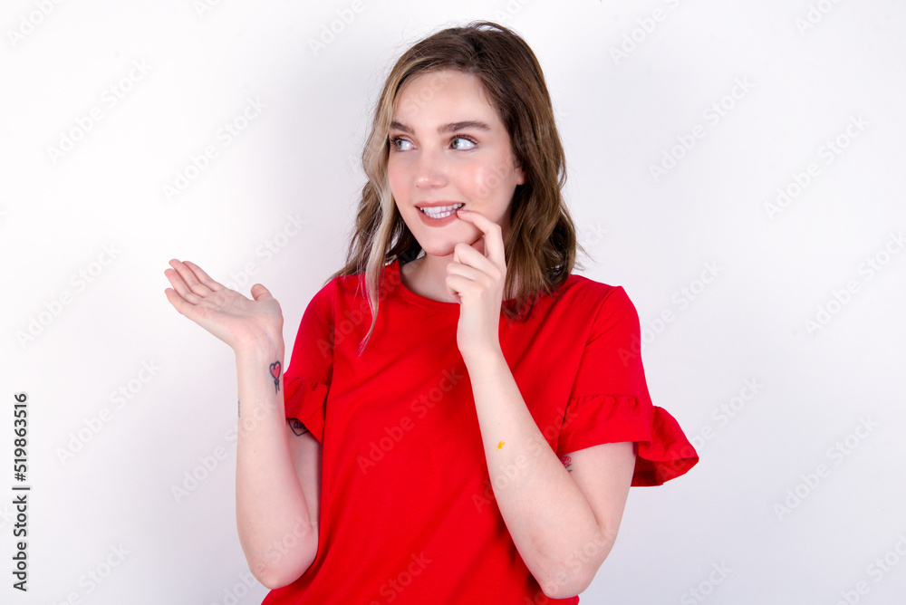 Positive young caucasian woman wearing red T-shirt over white background advert promo touches teeth with finger. Positive young caucasian woman wearing red T-shirt over white background advert promo touches teeth with finger.