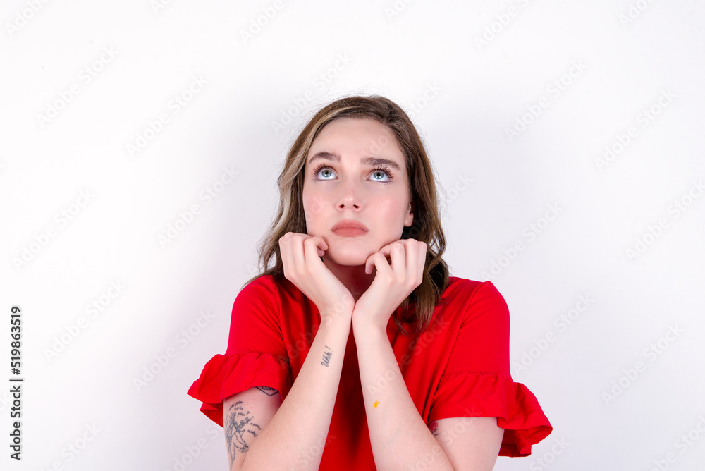 Portrait of sad young caucasian woman wearing red T-shirt over white background hands face look empty space Portrait of sad young caucasian woman wearing red T-shirt over white background hands face look empty space