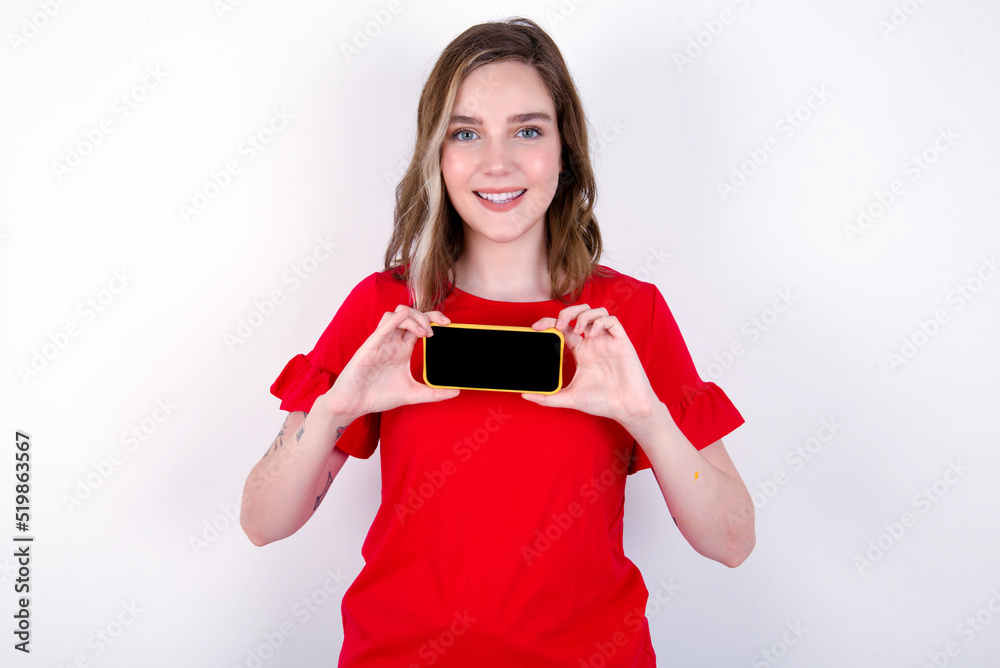 Cheerful cheery content young caucasian woman wearing red T-shirt over white background holding in hands device hobby smm post blog Cheerful cheery content young caucasian woman wearing red T-shirt over white background holding in hands device hobby smm post blog