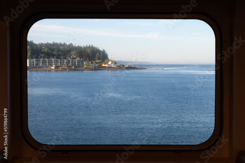 View through a rectangular ferry window of the Mukilteo shoreline and the blue water of Puget Sound