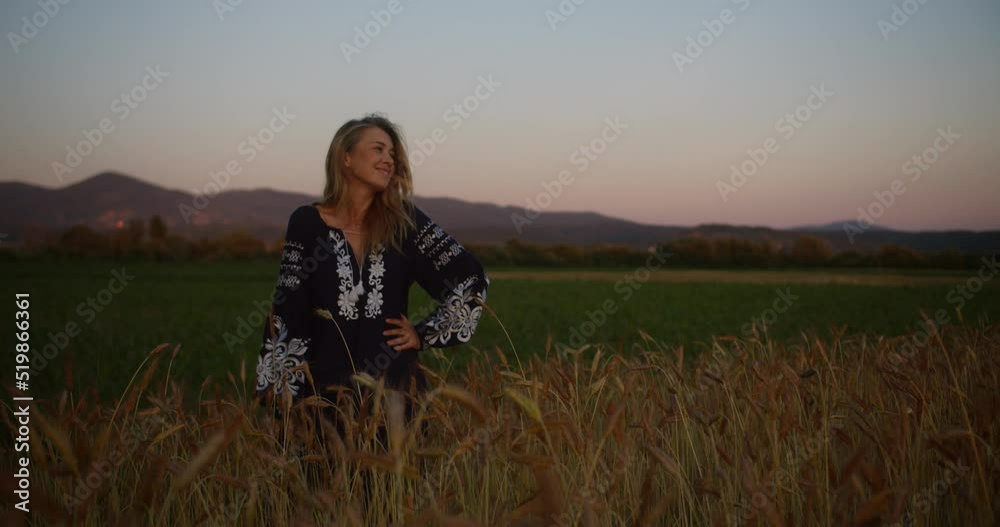Blond girl in national Ukrainian clothes - embroidery with long hair walking and standing in the yellow field of wheat at beautiful sunset. Wheat heads swinging in the evening breeze Blond girl in national Ukrainian clothes - embroidery with long hair walking and standing in the yellow field of wheat at beautiful sunset. Wheat heads swinging in the evening breeze