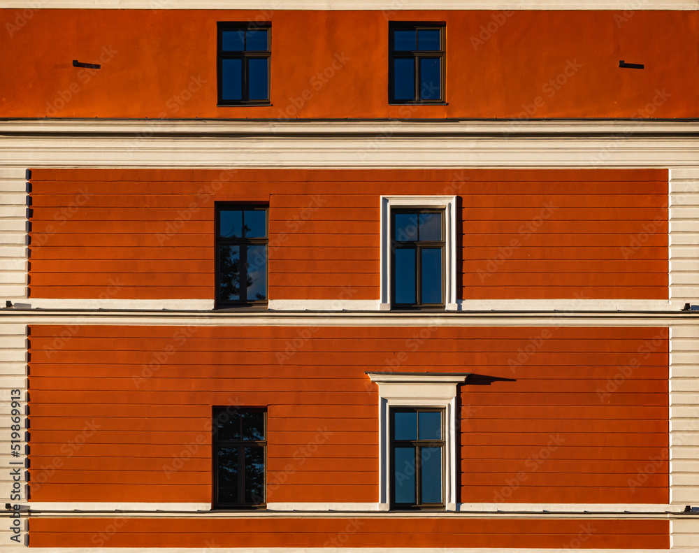 Six windows on a  dark orange wall with a white stripes. Exterior facade of dark orange historical house with apartments