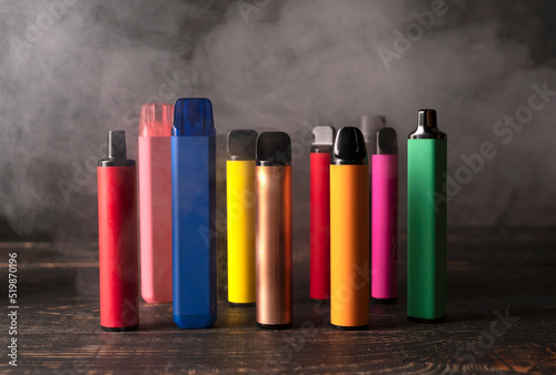 Set of colorful disposable electronic cigarettes on a dark wood background with smoke.