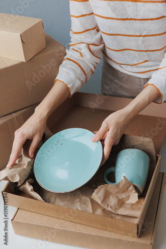 woman entrepreneur sells dishes, plates and cups made of clay, ceramics online and packs them in boxes for sending to the delivery service. small business selling goods on the Internet on the