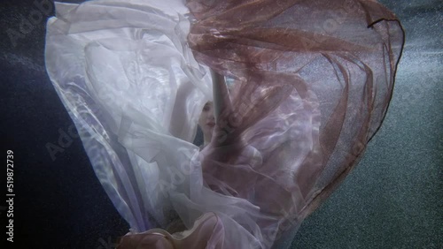 a red-haired woman appears from behind translucent fabrics in the dark under water