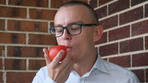 Young man eating fresh tomato, close-up photo