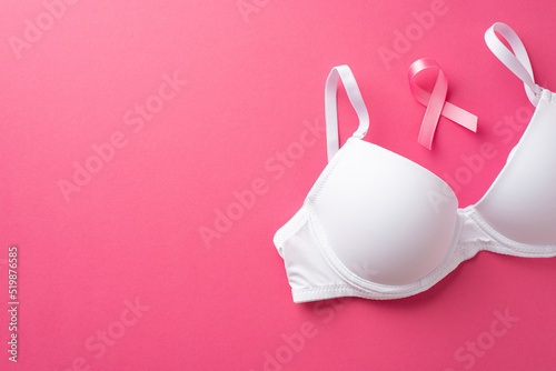 Breast cancer awareness concept. Top view photo of pink silk ribbon and white bra on isolated pink background with empty space