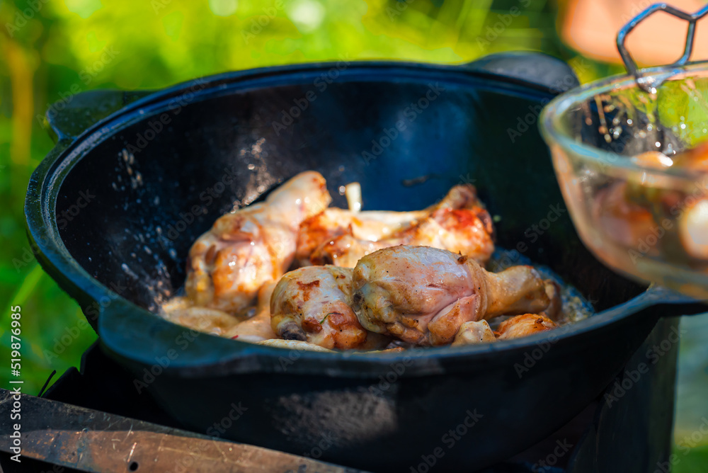 Fresh, juicy chicken legs are fried with onions in a cast-iron cauldron in vegetable oil. Georgian chakhokhbili with chicken. Small depth of field. Food in nature.