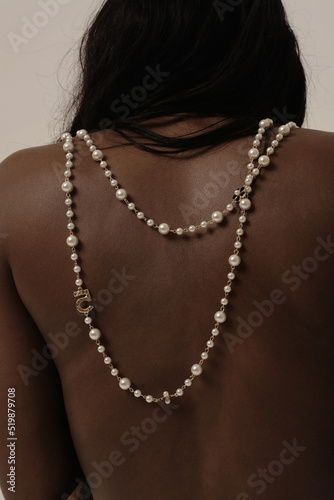 Close-up of beautiful woman with pearl necklace accessories on tan skin indoor.