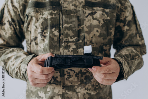 A military man demonstrates a combat medical tourniquet to stop blood during first aid. Instructions for combat tactical equipment.