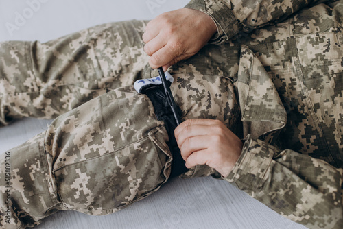 A military man demonstrates a combat medical tourniquet to stop blood during first aid. Instructions for combat tactical equipment.