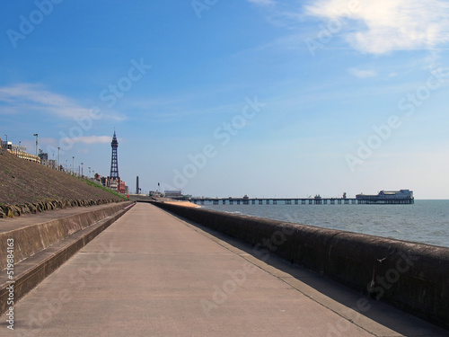 vertical perspective view along the pedestrian promenade in blackpool with a view of the town tower and pier in the distance with calm summer sea and blue sky © Philip J Openshaw 