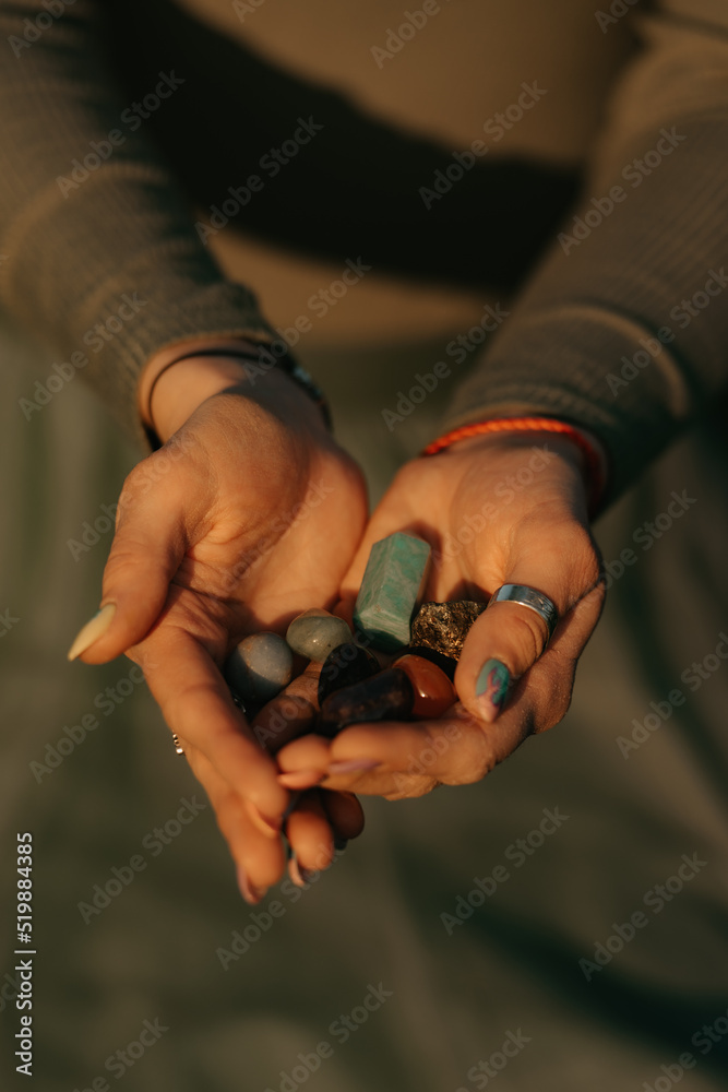 A close photo of a bunch of colorful stones in the hands of a woman for magical therapy. Session of a meditation healing in the park at sunset.