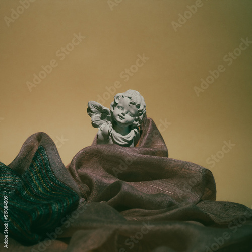 Sculpture of  angel and colorful silk scarf on background. Flat lay concept. photo