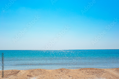 Blue sparkling sea with a strip of sandy shore and a clear blue sky on a sunny day