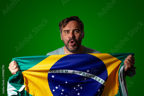 Male soccer fan holding a Brazilian flag. Background with lettering "Gol" in Portuguese like a soccer celebration