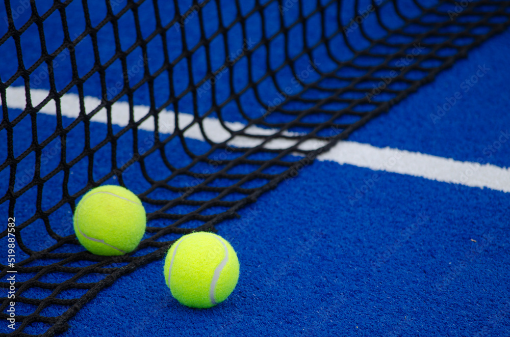 Blue paddle tennis court, two balls near the net